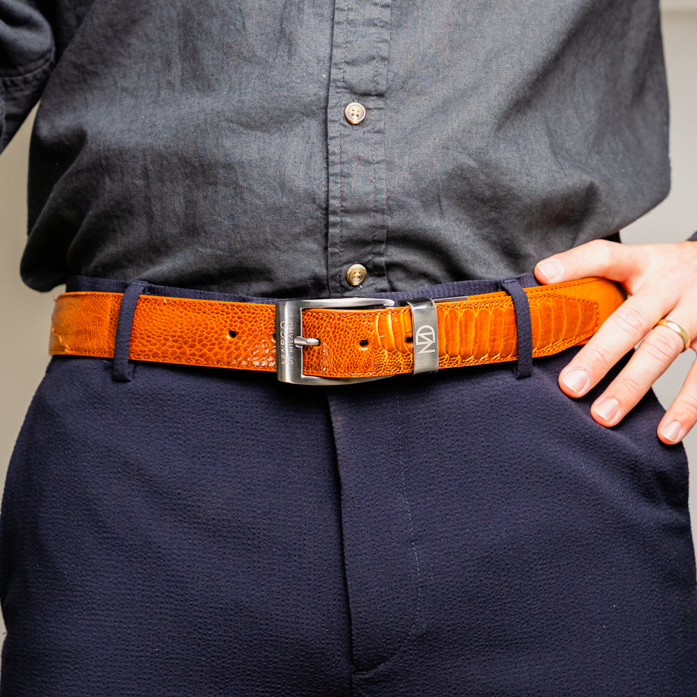A coiled Alessio Belt Cognac by Marco Di Milano, crafted from genuine ostrich leather in light brown with a textured pattern and a silver buckle engraved with the brand name.