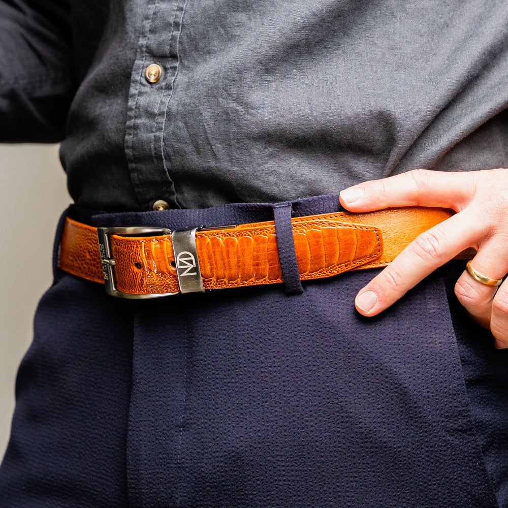 A coiled Alessio Belt Cognac by Marco Di Milano, crafted from genuine ostrich leather in light brown with a textured pattern and a silver buckle engraved with the brand name.