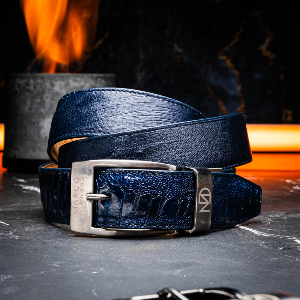 The Alessio Belt Navy by Marco Di Milano is a coiled blue handcrafted luxury belt with a silver buckle, featuring both smooth and textured crocodile-patterned sections.