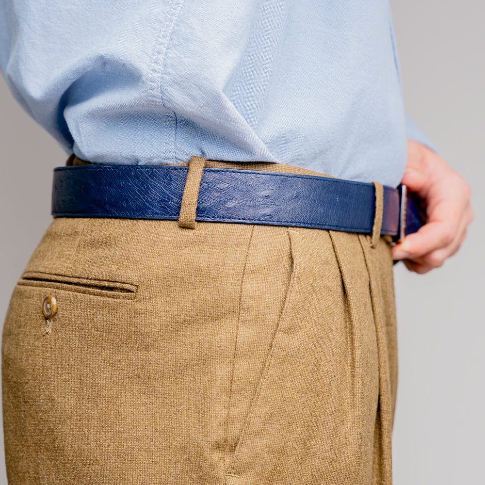 The Alessio Belt Navy by Marco Di Milano is a coiled blue handcrafted luxury belt with a silver buckle, featuring both smooth and textured crocodile-patterned sections.