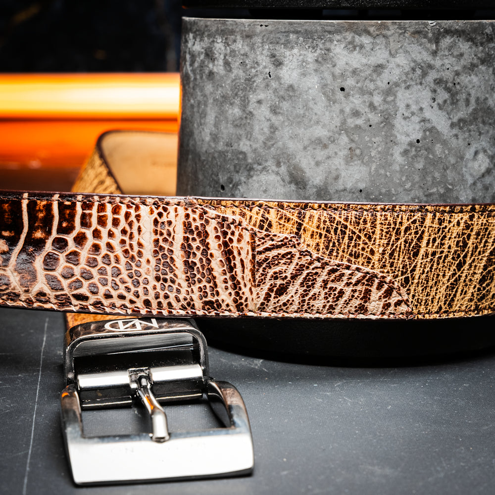 The Alessio Belt Orix by Marco Di Milano, featuring textured genuine ostrich leather in brown and a silver buckle, is coiled to display both its inside and outside surfaces.