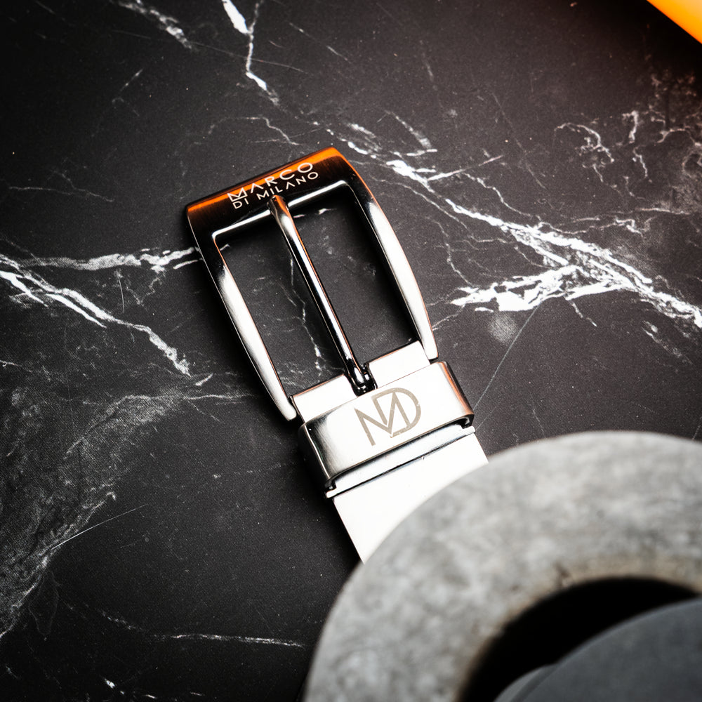 Introducing the Alessio Belt White / Gray by Marco Di Milano—a handcrafted luxury accessory featuring a textured gray exotic leather strap and a distinctive white, ridged front. The metallic buckle is engraved with the Marco Di Milano logo, accentuating the exquisite craftsmanship of this elegant belt.