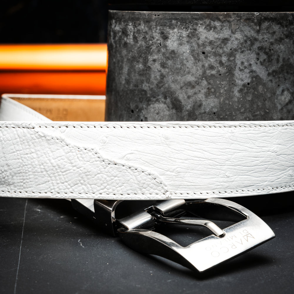 Introducing the Alessio Belt White by Marco Di Milano—a handcrafted luxury belt in pristine white leather, adorned with a silver buckle engraved with the brand’s iconic signature, elegantly coiled on a white background.