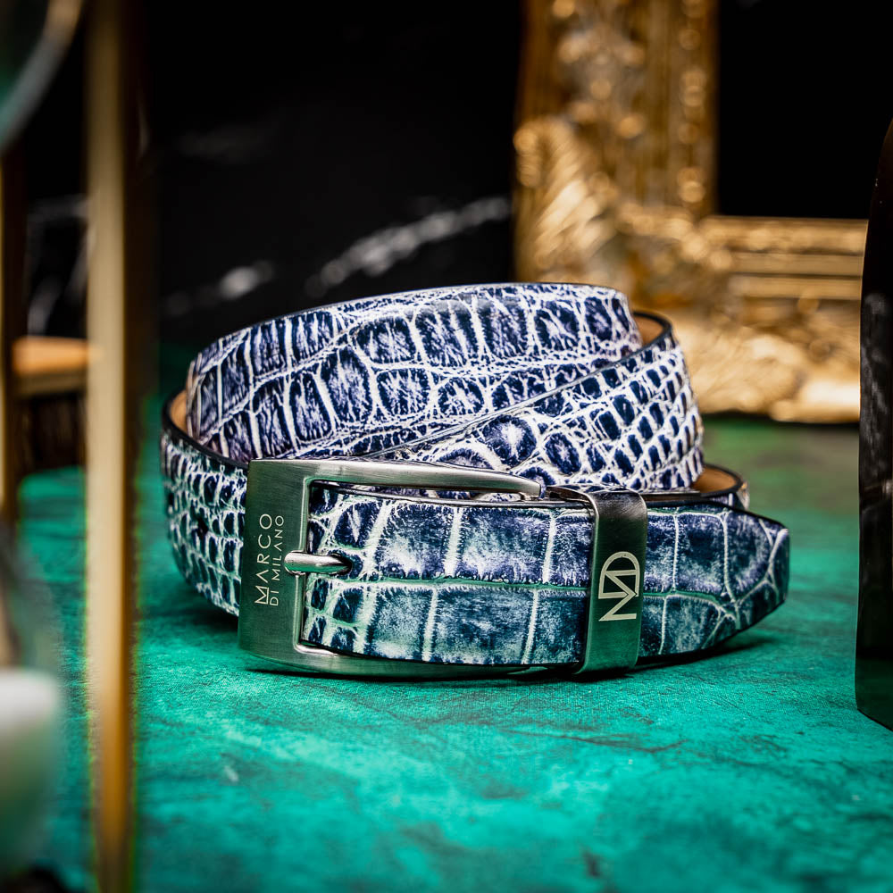 The Emilio Belt Antique Newspaper by Marco Di Milano features a rolled-up design with a silver buckle and textured black-and-white crocodile pattern, making it a standout accessory for those who appreciate exotic leather and refined style.