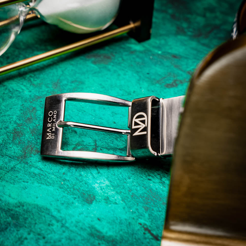 The Emilio Belt Antique Newspaper by Marco Di Milano features a rolled-up design with a silver buckle and textured black-and-white crocodile pattern, making it a standout accessory for those who appreciate exotic leather and refined style.