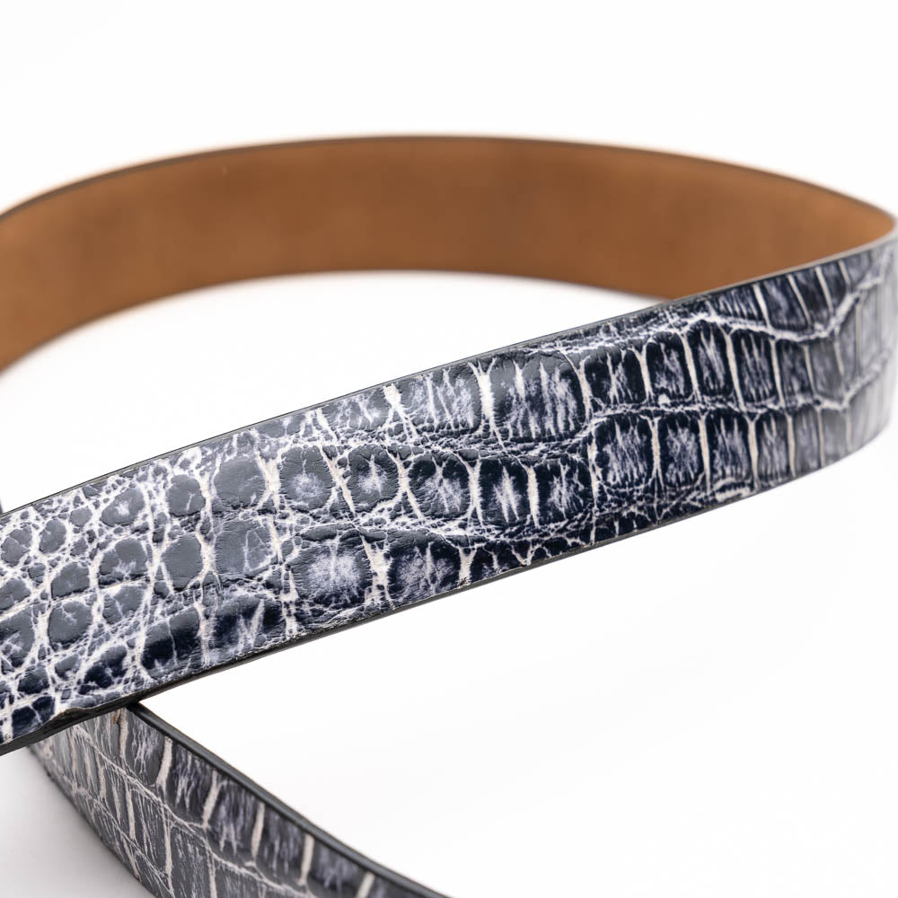The Emilio Belt Antique Newspaper by Marco Di Milano features a rolled-up design with a silver buckle and textured black-and-white crocodile pattern, making it a standout accessory for those who appreciate exotic leather and refined style.