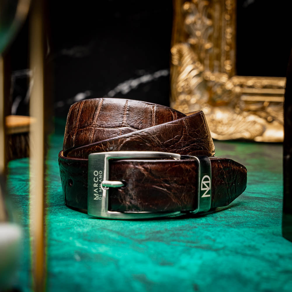 The Emilio Belt Brown by Marco Di Milano is a dark brown genuine alligator belt with a silver "Marco Donini" engraved buckle, coiled on a white background—designed to perfectly complement Marco Di Milano luxury footwear.