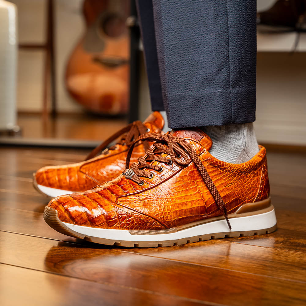 The Alonzo Cognac sneaker by Marco Di Milano features a hand-painted brown caiman crocodile-patterned leather upper and a white-brown rubber sole—luxury footwear for discerning tastes, shown in a sleek side view.