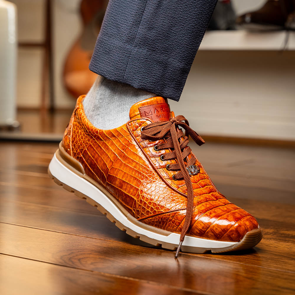 The Alonzo Cognac sneaker by Marco Di Milano features a hand-painted brown caiman crocodile-patterned leather upper and a white-brown rubber sole—luxury footwear for discerning tastes, shown in a sleek side view.
