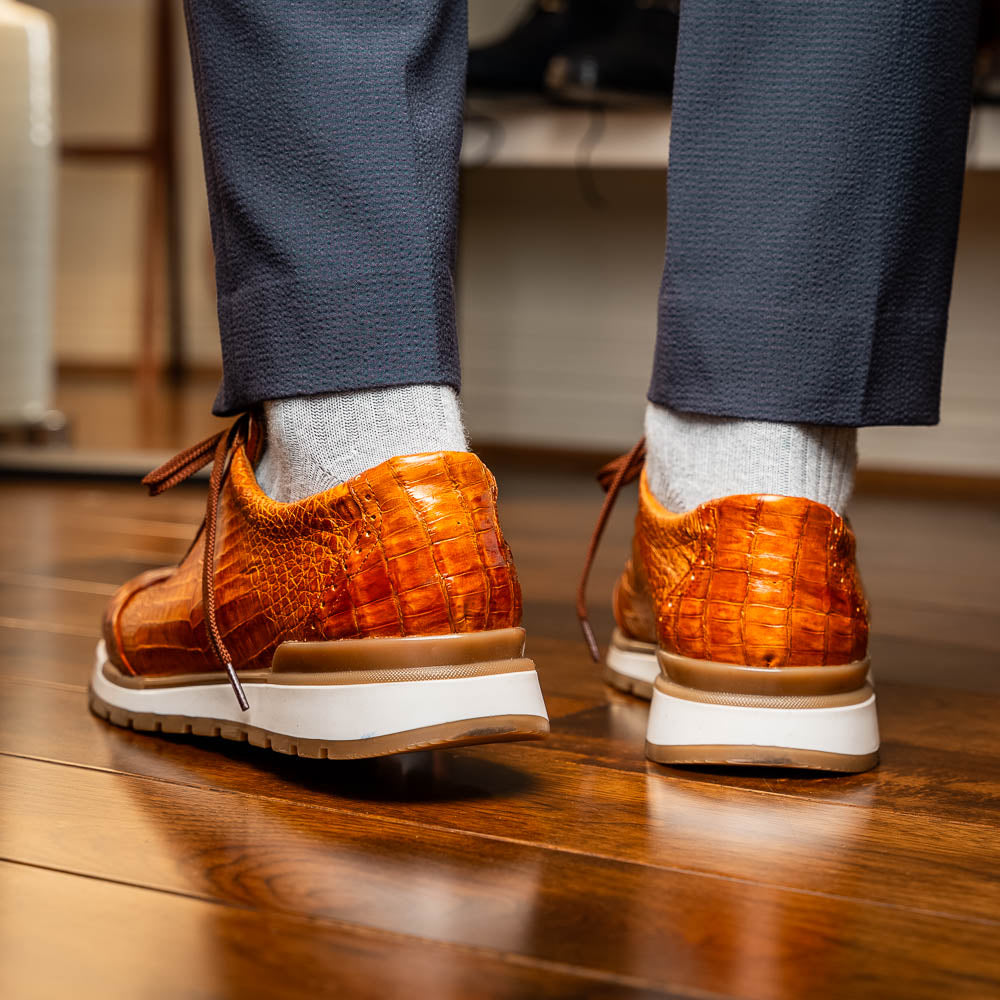 The Alonzo Cognac sneaker by Marco Di Milano features a hand-painted brown caiman crocodile-patterned leather upper and a white-brown rubber sole—luxury footwear for discerning tastes, shown in a sleek side view.