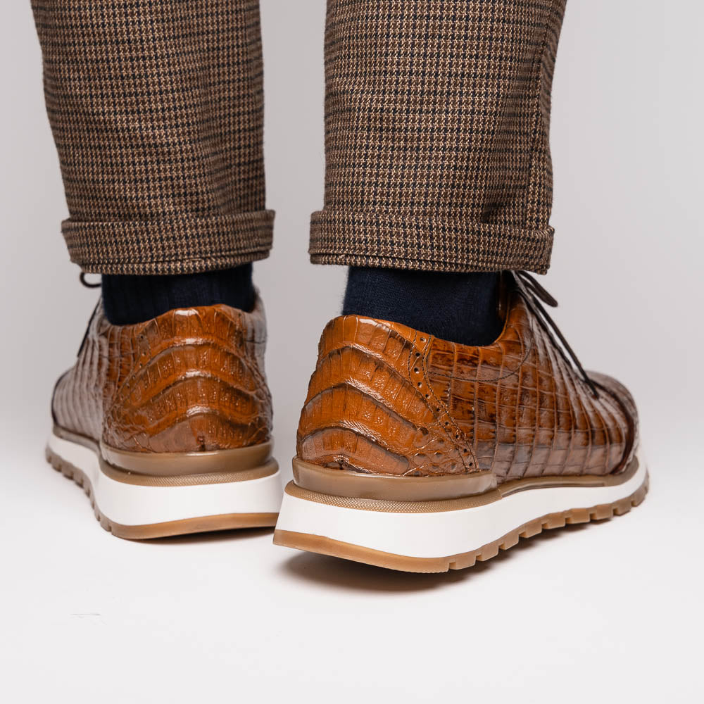 The Marco Di Milano Alonzo Bay Apache sneakers feature brown genuine caiman crocodile leather, white midsoles, brown rubber outsoles, a lace-up design, and a textured pattern—luxury footwear ideal for any occasion.