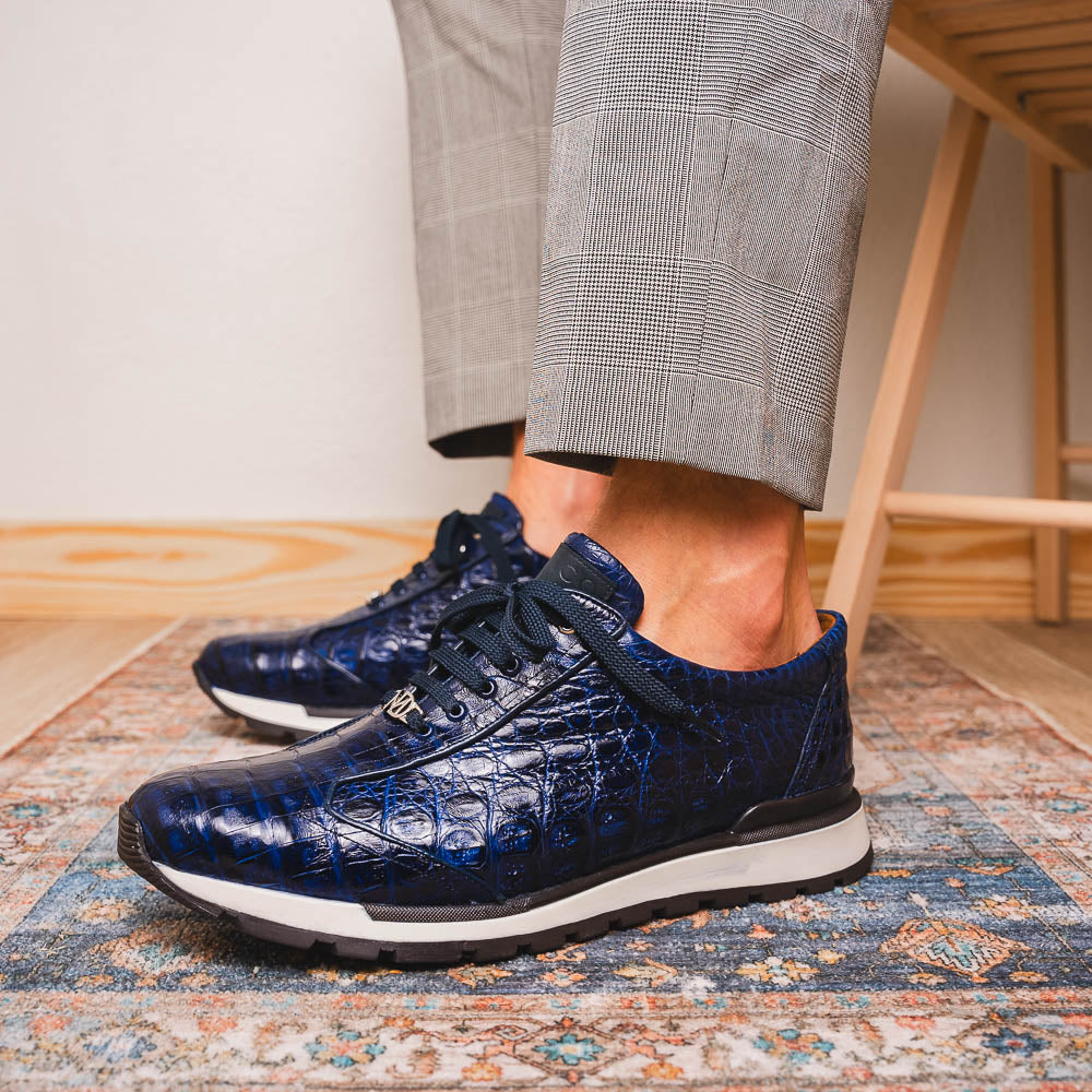 The Alonzo Navy by Marco Di Milano is a luxury men's sneaker in genuine caiman crocodile leather, featuring black laces, a hand-painted finish, white midsole, and black textured outsole.