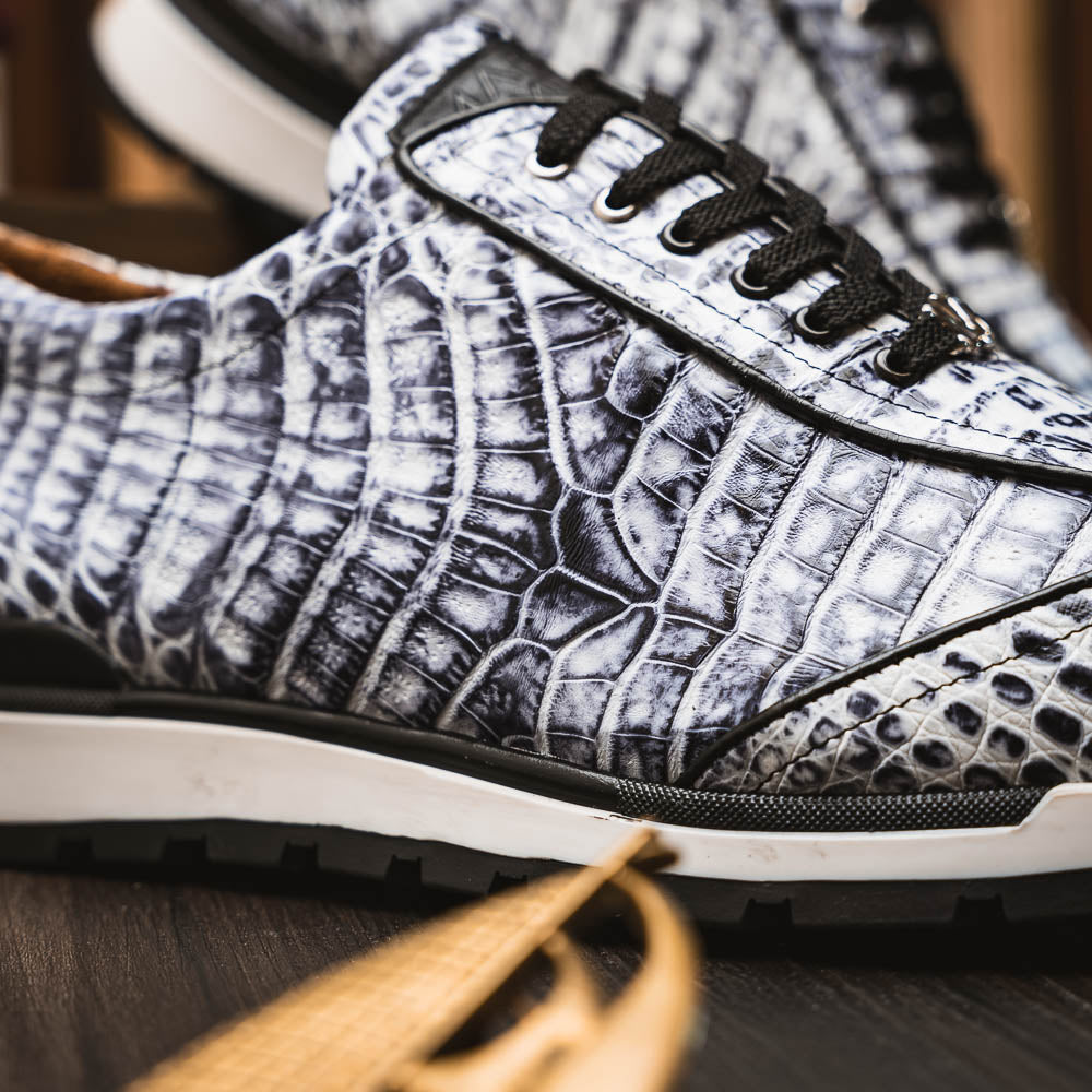 The Alonzo Newspaper sneakers by Marco Di Milano feature genuine caiman crocodile in white and black with a hand-painted finish, black laces, and black rubber soles, displayed with one shoe propped on the other against a white background.