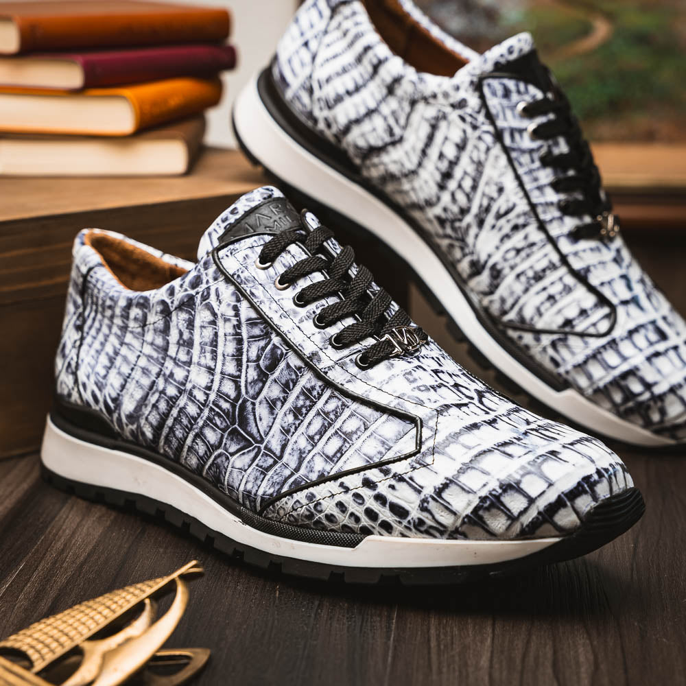 The Alonzo Newspaper sneakers by Marco Di Milano feature genuine caiman crocodile in white and black with a hand-painted finish, black laces, and black rubber soles, displayed with one shoe propped on the other against a white background.