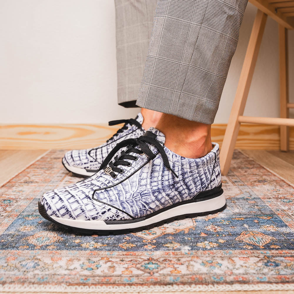 The Alonzo Newspaper sneakers by Marco Di Milano feature genuine caiman crocodile in white and black with a hand-painted finish, black laces, and black rubber soles, displayed with one shoe propped on the other against a white background.