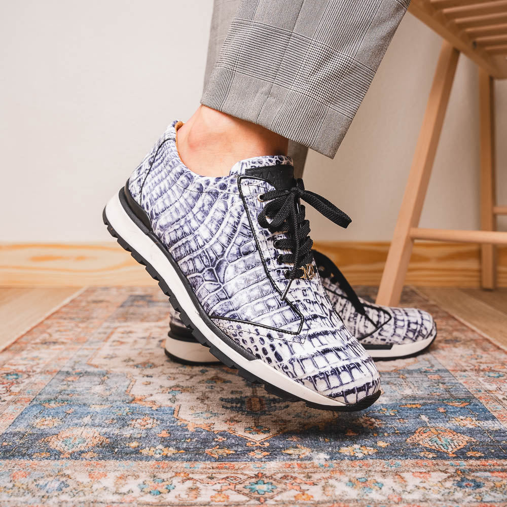The Alonzo Newspaper sneakers by Marco Di Milano feature genuine caiman crocodile in white and black with a hand-painted finish, black laces, and black rubber soles, displayed with one shoe propped on the other against a white background.