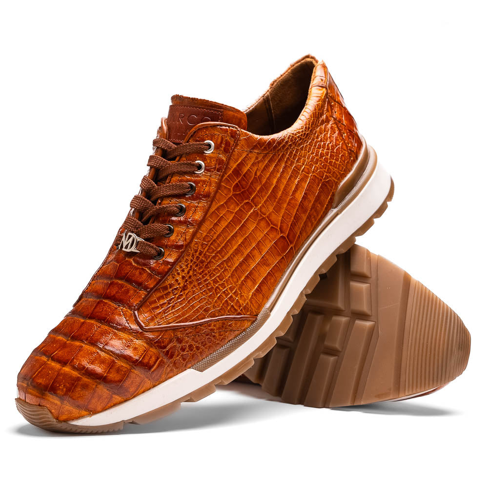 The Alonzo Cognac by Marco Di Milano is a luxury men's sneaker with brown genuine caiman crocodile leather, white midsoles, and brown rubber outsoles. One shoe stands upright while the other displays its hand-painted sole.
