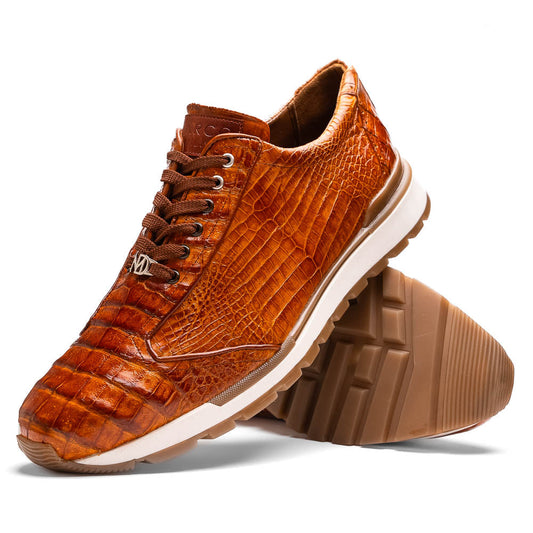 The Alonzo Cognac by Marco Di Milano is a luxury men's sneaker with brown genuine caiman crocodile leather, white midsoles, and brown rubber outsoles. One shoe stands upright while the other displays its hand-painted sole.