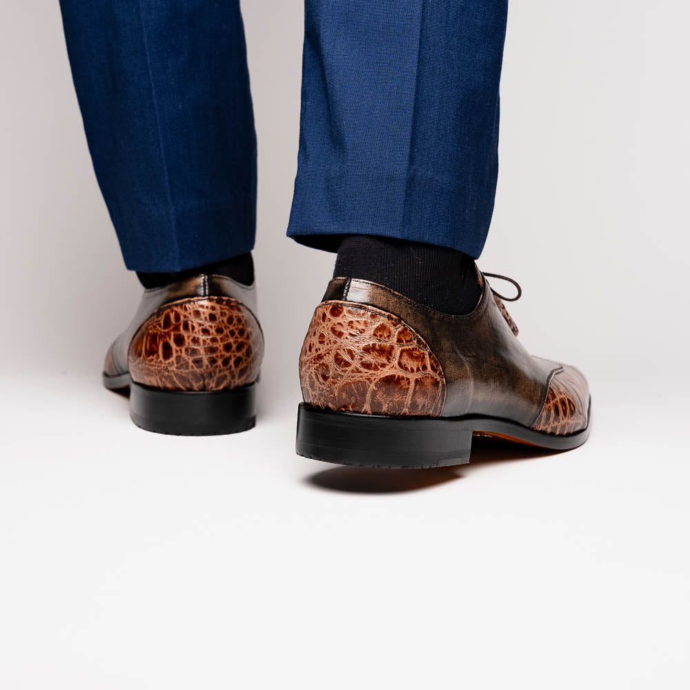 A pair of Anzio Rustic Orix brown leather dress shoes by Marco Di Milano, featuring a textured crocodile pattern—one upright, the other showing a smooth tan sole—represent true luxury men's footwear.