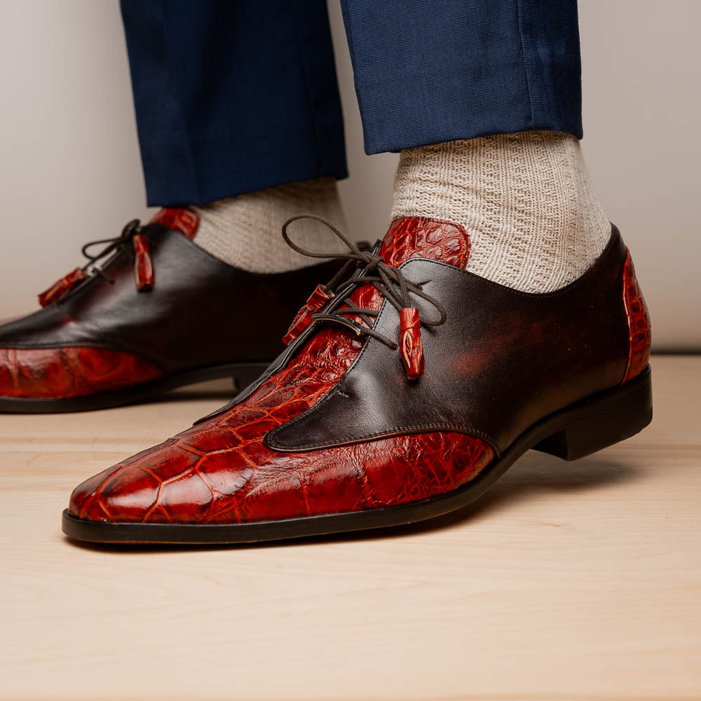 The Anzio Rustic Cognac by Marco Di Milano is a men's dress shoe featuring red and brown crocodile-patterned leather, lace-up closure, tassel accents, and leather soles—an elevated choice in luxury footwear.