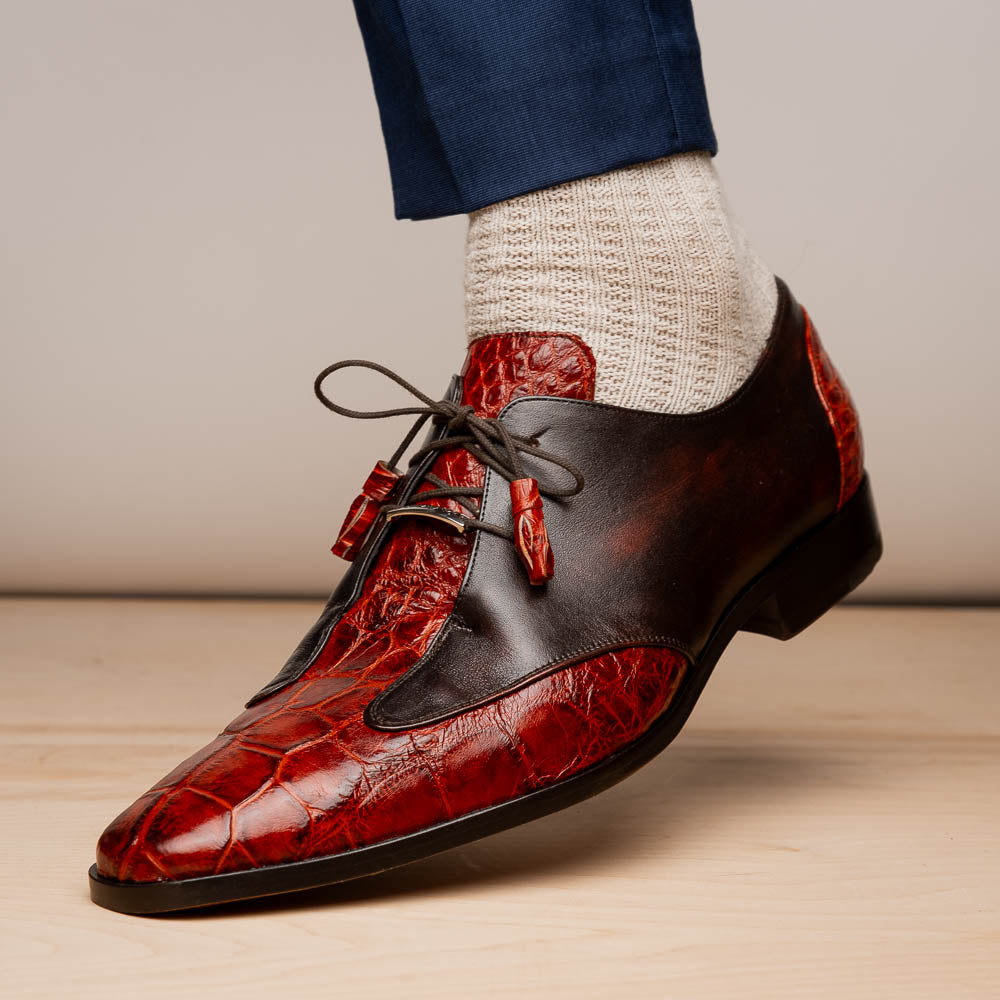 The Anzio Rustic Cognac by Marco Di Milano is a men's dress shoe featuring red and brown crocodile-patterned leather, lace-up closure, tassel accents, and leather soles—an elevated choice in luxury footwear.