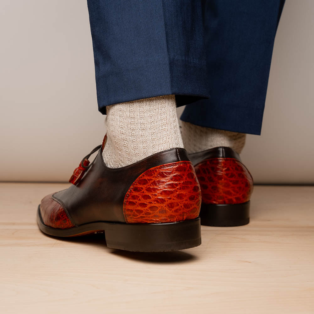 The Anzio Rustic Cognac by Marco Di Milano is a men's dress shoe featuring red and brown crocodile-patterned leather, lace-up closure, tassel accents, and leather soles—an elevated choice in luxury footwear.