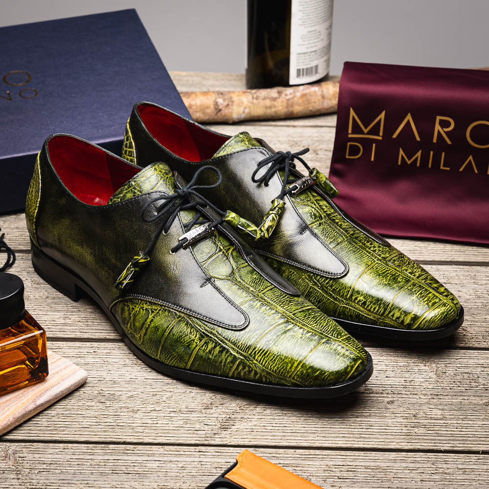 A pair of Anzio Rustic Green men's dress shoes by Marco Di Milano, featuring a green textured finish, black laces, and brown leather soles—one upright and one lying on its side.