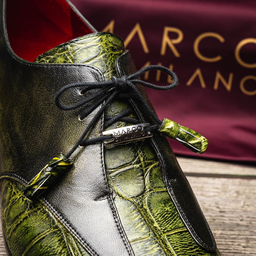 A pair of Anzio Rustic Green men's dress shoes by Marco Di Milano, featuring a green textured finish, black laces, and brown leather soles—one upright and one lying on its side.