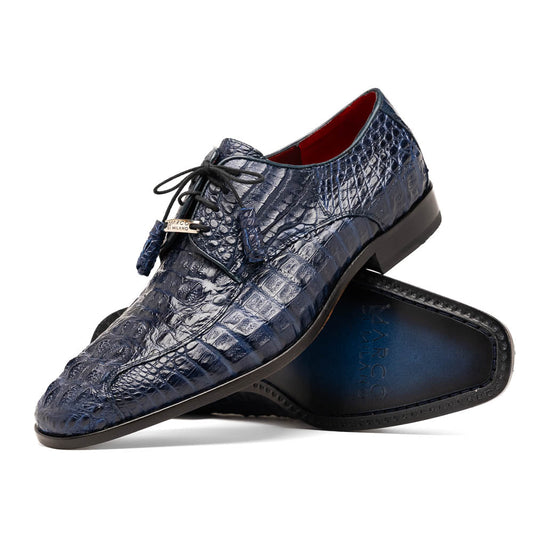 A pair of Marco Di Milano Apricena Midnight shoes—genuine dark blue caiman crocodile with black laces and a metal accent, one upright and one on its side highlighting the sole—offers a refined choice in luxury men's footwear.