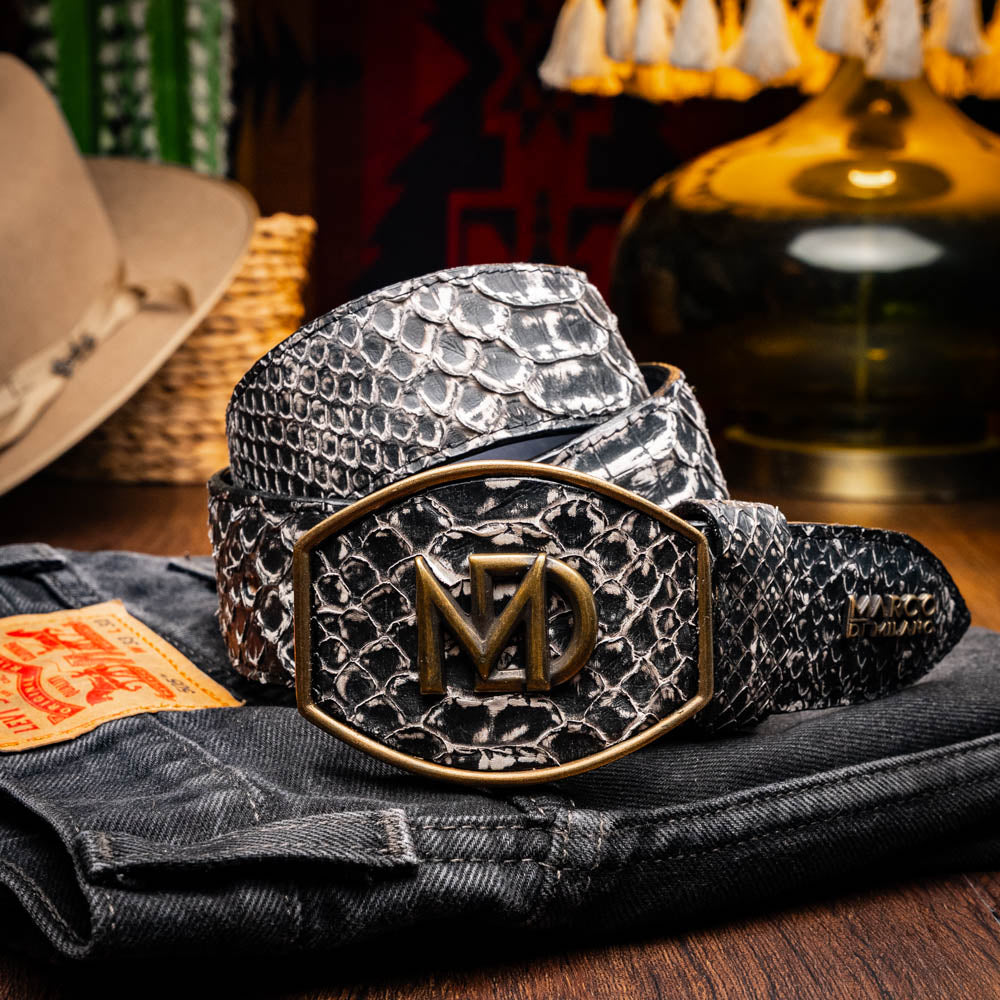 The Arkansas Belt Antique Newspaper by Marco Di Milano features genuine python skin in black and silver, a large gold “MD” buckle, and “MARCO MILANO” text on the tip, fusing exotic style with luxury craftsmanship.