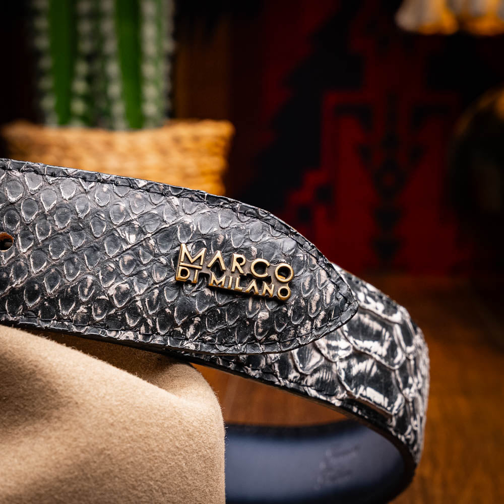 The Arkansas Belt Antique Newspaper by Marco Di Milano features genuine python skin in black and silver, a large gold “MD” buckle, and “MARCO MILANO” text on the tip, fusing exotic style with luxury craftsmanship.