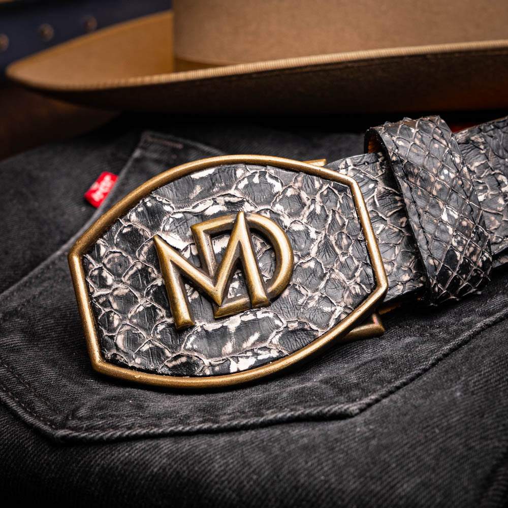 The Arkansas Belt Antique Newspaper by Marco Di Milano features genuine python skin in black and silver, a large gold “MD” buckle, and “MARCO MILANO” text on the tip, fusing exotic style with luxury craftsmanship.