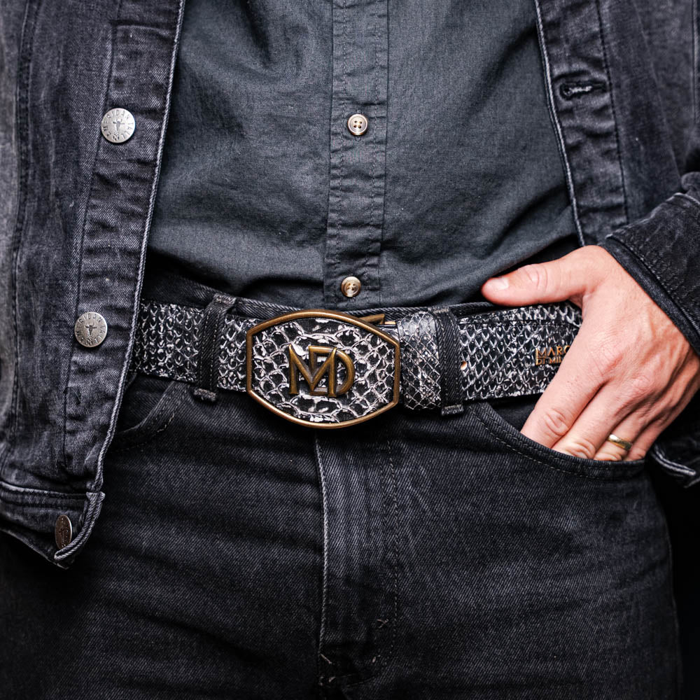 The Arkansas Belt Antique Newspaper by Marco Di Milano features genuine python skin in black and silver, a large gold “MD” buckle, and “MARCO MILANO” text on the tip, fusing exotic style with luxury craftsmanship.
