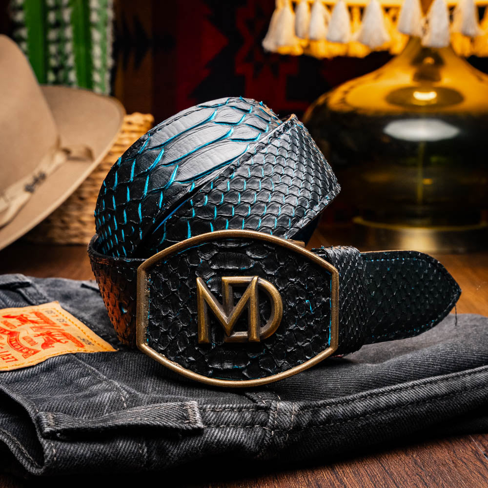 The Arkansas Belt Black / Blue by Marco Di Milano features a handcrafted black snakeskin pattern and a gold and black "MD" buckle, displayed against a white background.