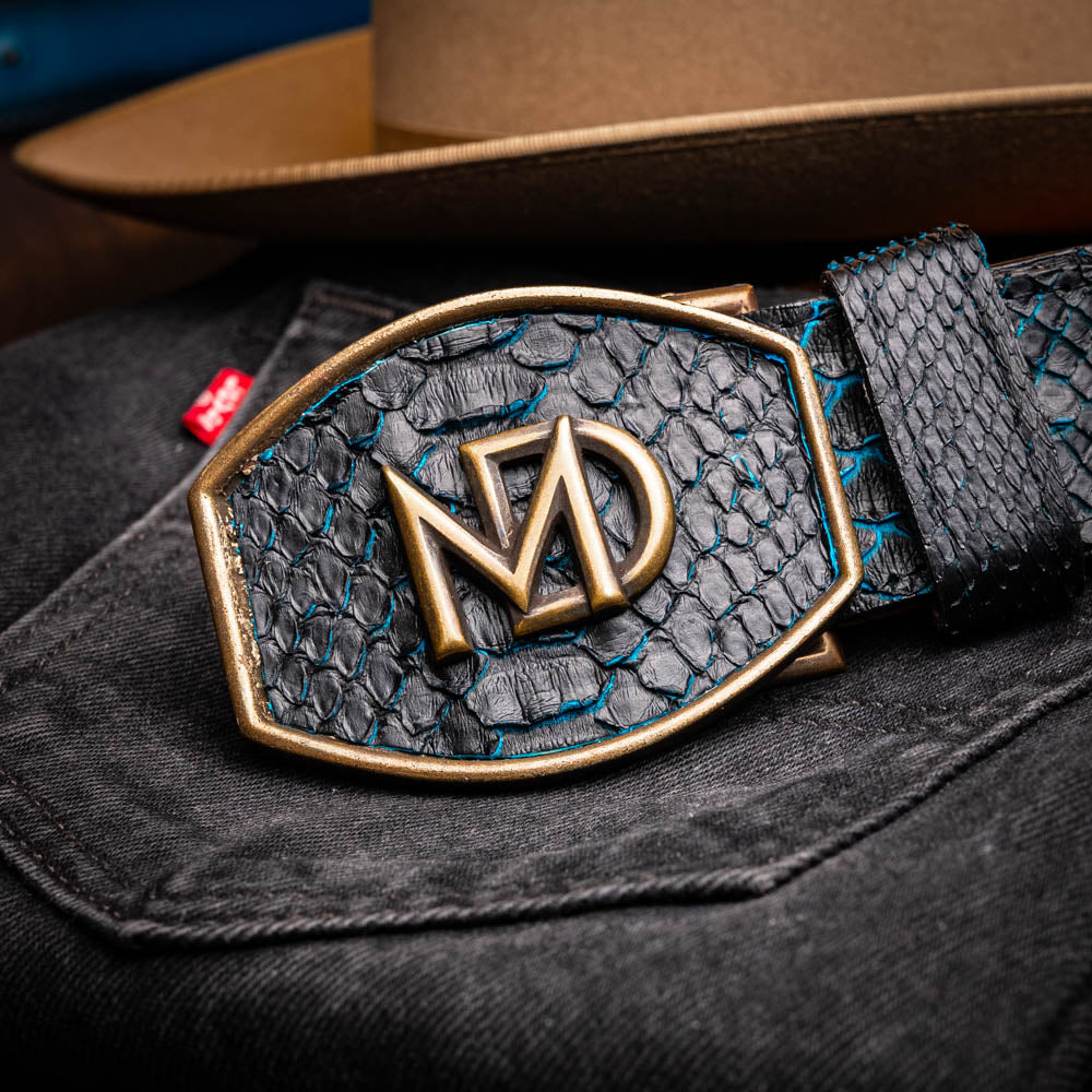The Arkansas Belt Black / Blue by Marco Di Milano features a handcrafted black snakeskin pattern and a gold and black "MD" buckle, displayed against a white background.