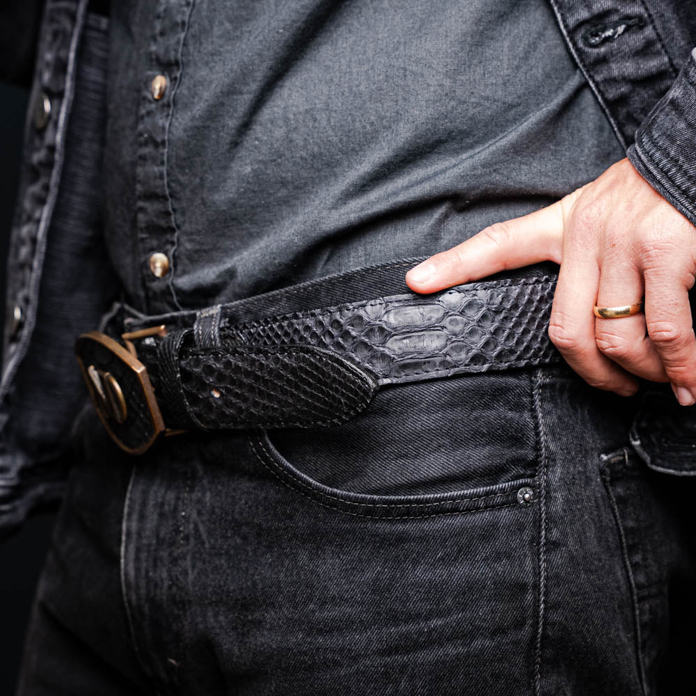 The Arkansas Belt Black / Blue by Marco Di Milano features a handcrafted black snakeskin pattern and a gold and black "MD" buckle, displayed against a white background.