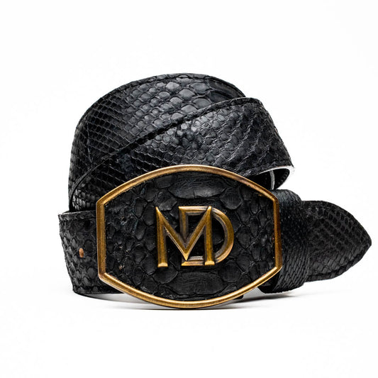 The Arkansas Belt Black by Marco Di Milano features textured black leather and a gold MD monogram buckle, shown coiled on a white background.