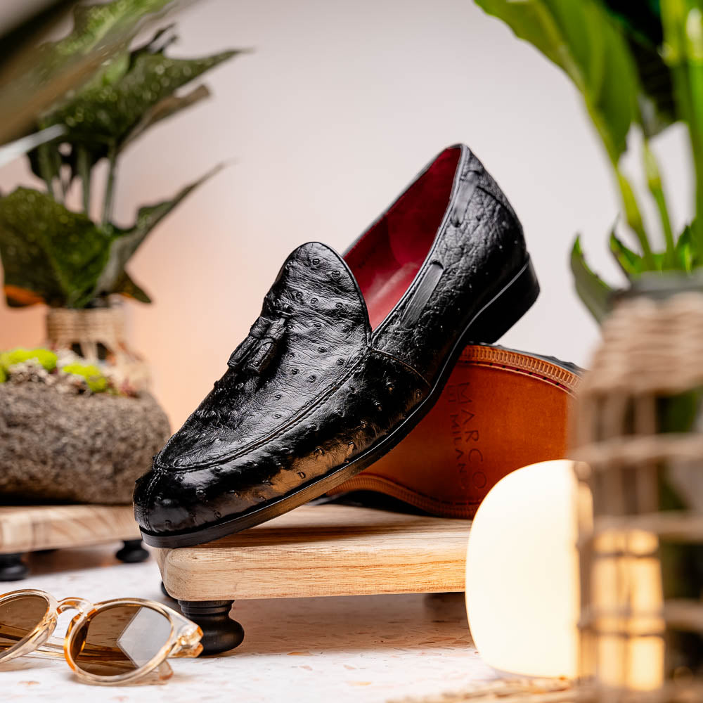 The Aubiere Black by Marco Di Milano are luxury men's tassel loafers in black genuine ostrich leather, shown with one shoe upright and the other displaying a tan sole embossed with the Marco Di Milano logo.