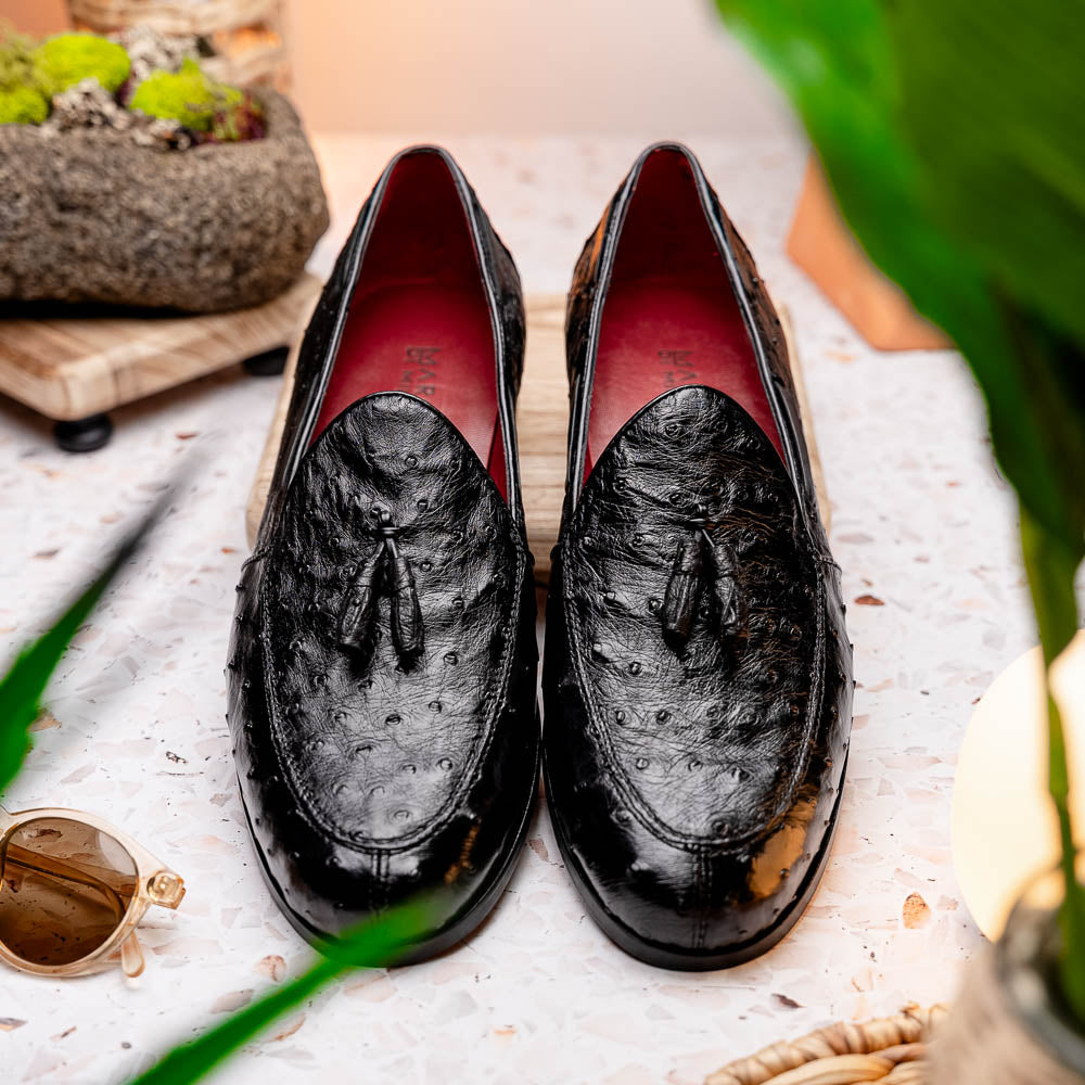 The Aubiere Black by Marco Di Milano are luxury men's tassel loafers in black genuine ostrich leather, shown with one shoe upright and the other displaying a tan sole embossed with the Marco Di Milano logo.