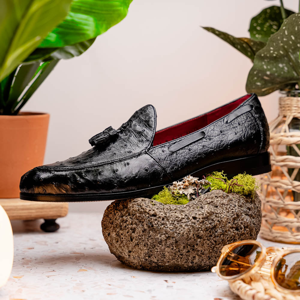 The Aubiere Black by Marco Di Milano are luxury men's tassel loafers in black genuine ostrich leather, shown with one shoe upright and the other displaying a tan sole embossed with the Marco Di Milano logo.