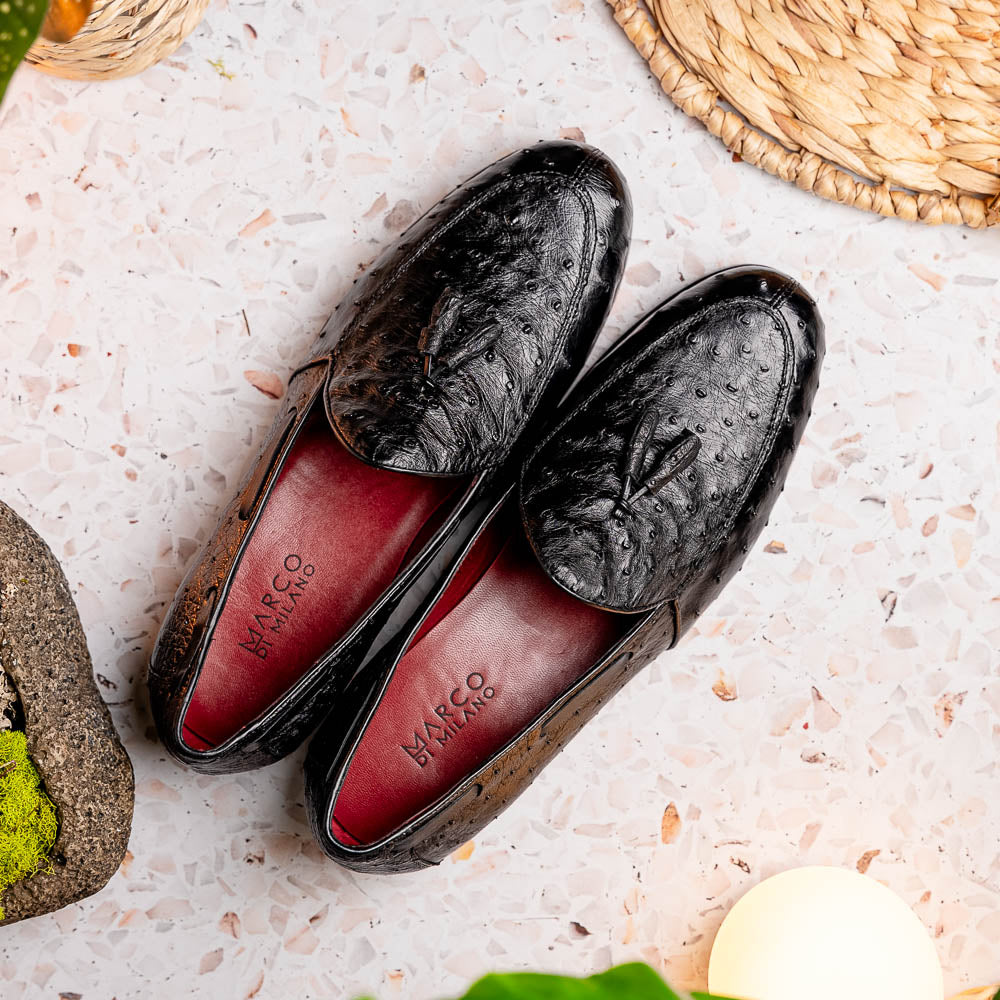The Aubiere Black by Marco Di Milano are luxury men's tassel loafers in black genuine ostrich leather, shown with one shoe upright and the other displaying a tan sole embossed with the Marco Di Milano logo.