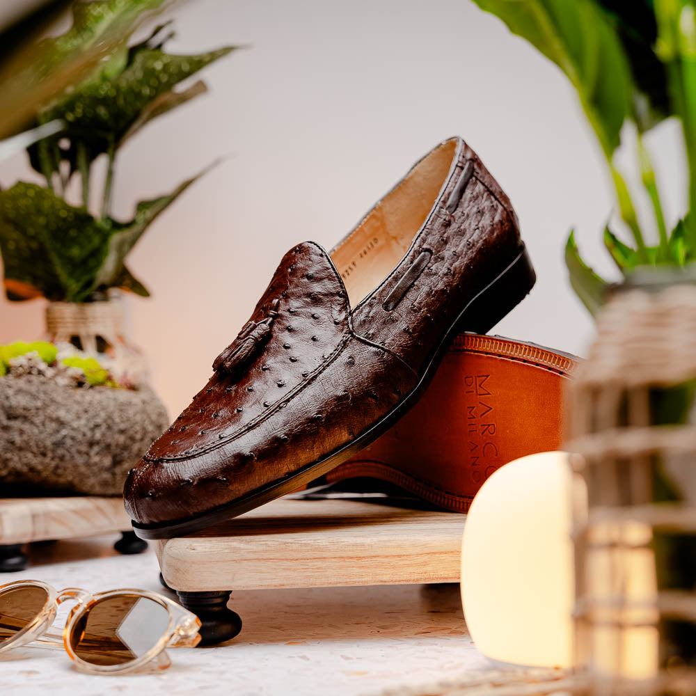 A pair of Marco Di Milano Aubiere Brown men's loafers, featuring brown leather with a textured pattern and tassel detail; one shoe stands upright while the other lies on its side showing the branded sole.