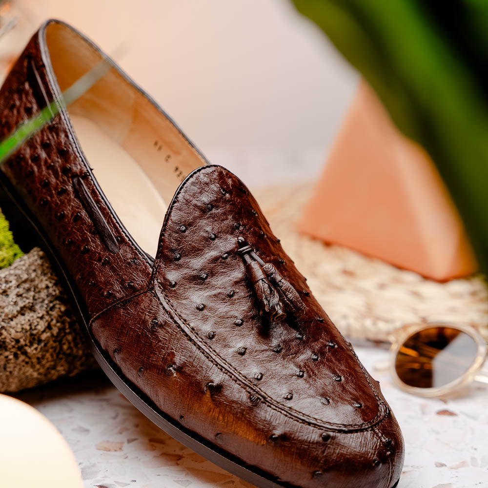 A pair of Marco Di Milano Aubiere Brown men's loafers, featuring brown leather with a textured pattern and tassel detail; one shoe stands upright while the other lies on its side showing the branded sole.