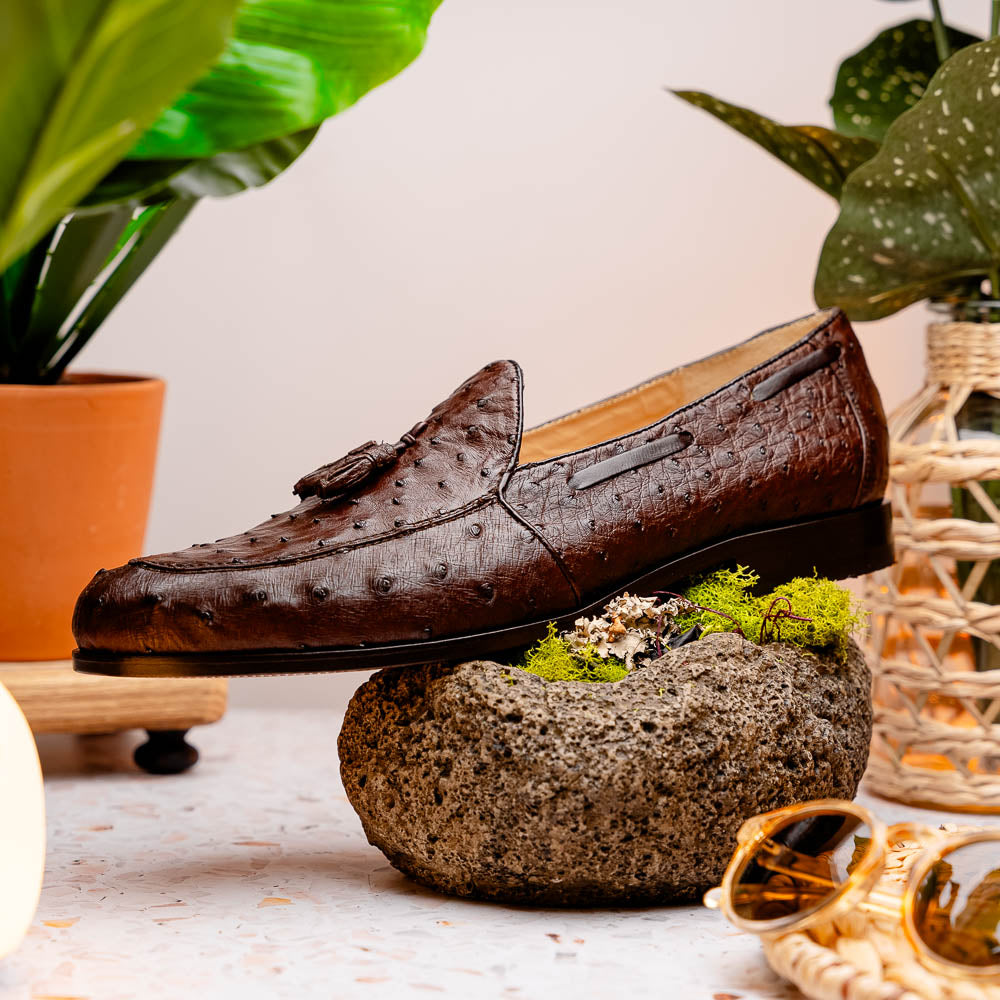 A pair of Marco Di Milano Aubiere Brown men's loafers, featuring brown leather with a textured pattern and tassel detail; one shoe stands upright while the other lies on its side showing the branded sole.