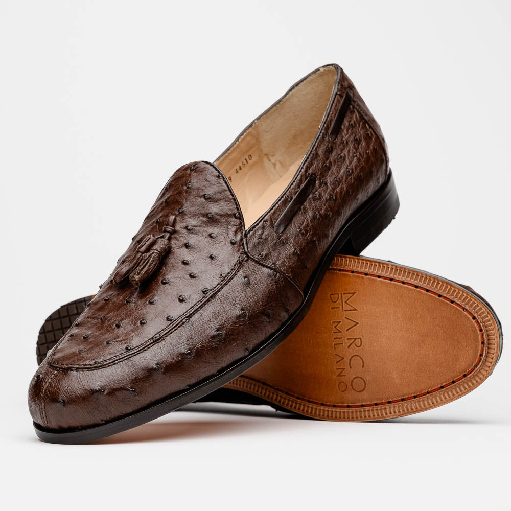 A pair of Marco Di Milano Aubiere Brown men's loafers, featuring brown leather with a textured pattern and tassel detail; one shoe stands upright while the other lies on its side showing the branded sole.