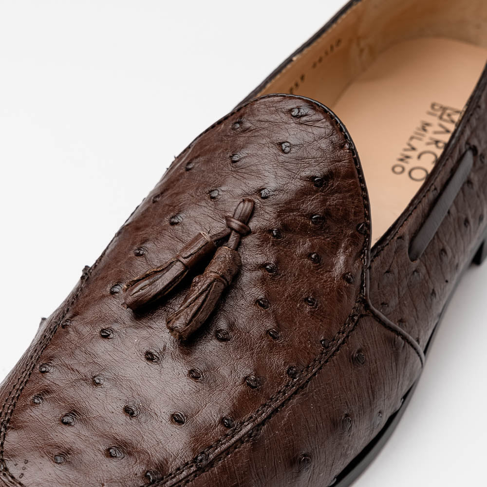 A pair of Marco Di Milano Aubiere Brown men's loafers, featuring brown leather with a textured pattern and tassel detail; one shoe stands upright while the other lies on its side showing the branded sole.