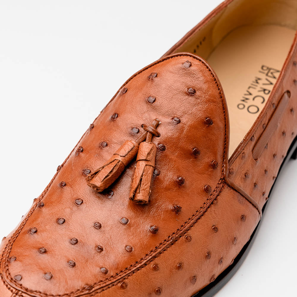 A pair of luxury men's footwear—Aubiere Cognac loafers by Marco Di Milano—boasts rich brown ostrich leather, with one shoe upright and the other on its side to reveal a sole stamped "Marco Di Milano.