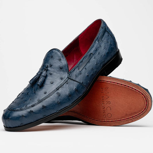A pair of luxury men's footwear: the Aubiere Navy by Marco Di Milano—blue ostrich tassel loafers with red inner lining and brown leather soles, one shoe propped to display the sole branding.