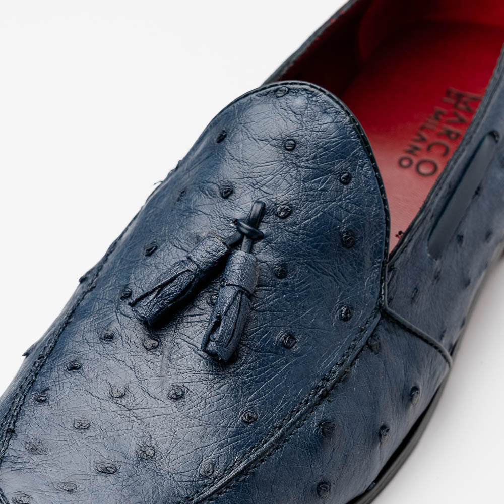 A pair of luxury men's footwear: the Aubiere Navy by Marco Di Milano—blue ostrich tassel loafers with red inner lining and brown leather soles, one shoe propped to display the sole branding.