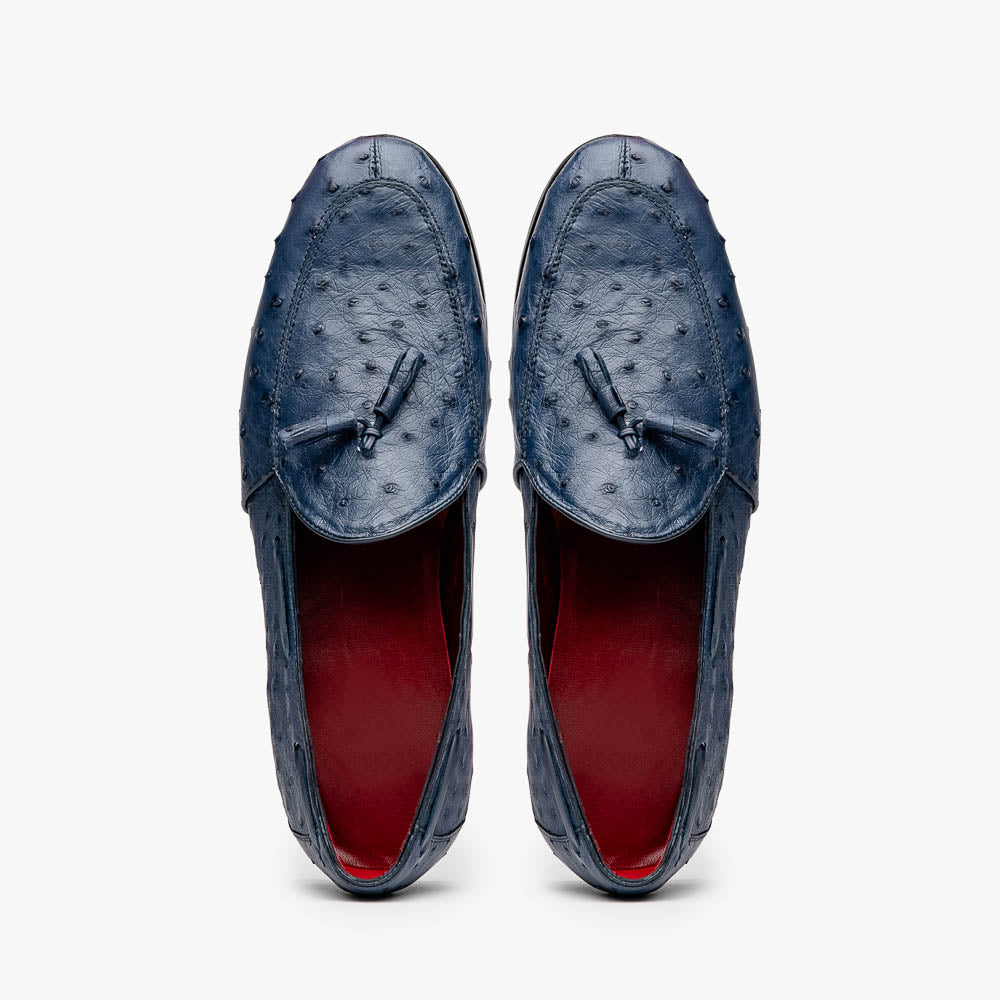 A pair of luxury men's footwear: the Aubiere Navy by Marco Di Milano—blue ostrich tassel loafers with red inner lining and brown leather soles, one shoe propped to display the sole branding.